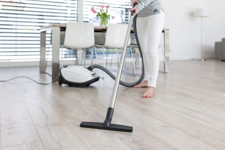 Woman using a vacuum cleaner to clean a wooden floor